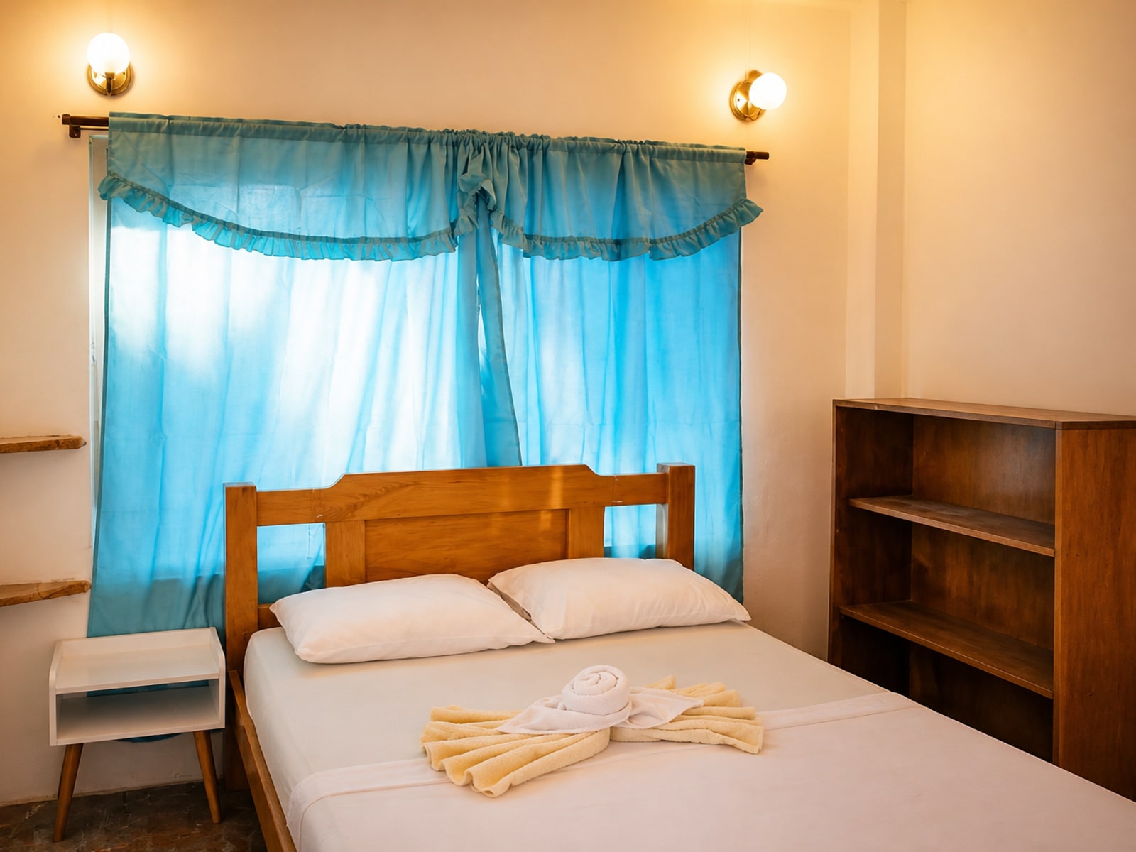 Habitación doble con cortinas azules, sábanas blancas y toallas decorativas